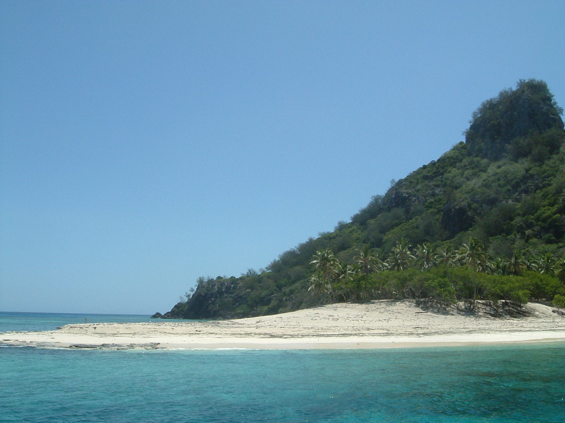 Monuriki island seen from the water, white sand beach below a green rocky peak.