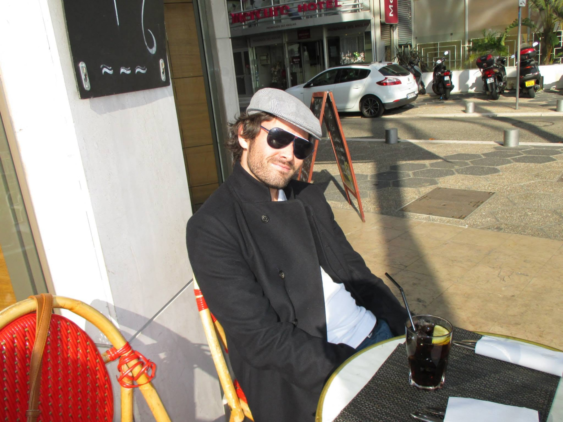 Nigel in a flat cap and sunglasses at a pavement café on the Promenade des Anglais in Nice.